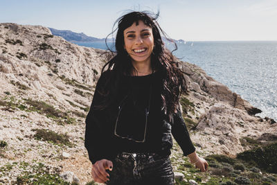 Portrait of smiling young woman standing against sea