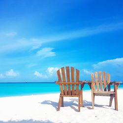 Wooden chairs on beach against blue sky