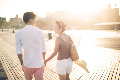 Rear view of couple holding hands while walking on pier