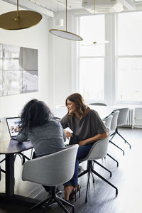 Female colleagues discussing over laptop computer in conference room at creative office