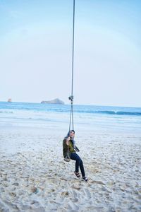 Woman wearing hijab swinging at beach against clear sky