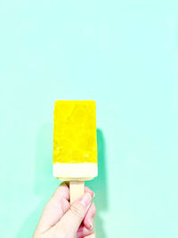 Cropped hand holding ice bar against blue background