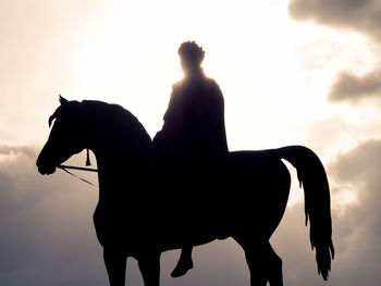Low angle view of silhouette man riding horse against sky