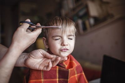 Middle aged father cutting hair to his son by himself at home looking video broadcast on laptop