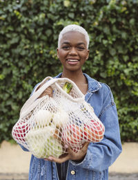 Smiling woman holding mesh bag with groceries