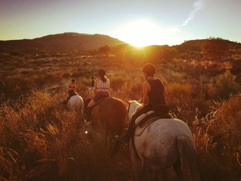 Rear view of mother with children horseback riding on field during sunset