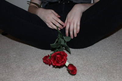 Midsection of woman with red rose relaxing on floor