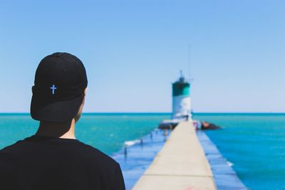 Rear view of man standing by lighthouse against clear blue sky