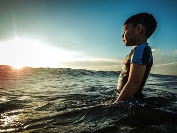 Side view of boy standing in sea against sky