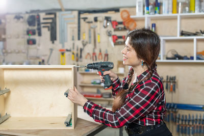 Side view of woman holding camera while standing at home