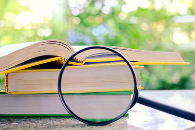 Close-up of magnifying glass by stack of books on table