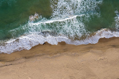 Aerial view of ocean waves washing a secluded sandy shoreline beach
