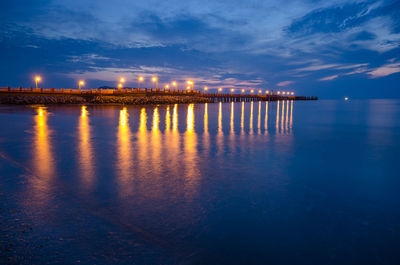 Illuminated pier over sea against during sunset