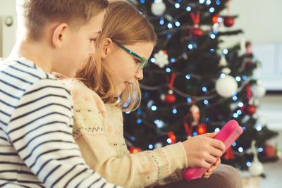 Siblings using digital tablet at home during christmas