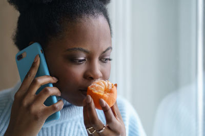 Close-up of woman smelling orange while talking on phone