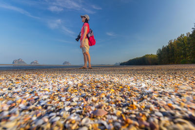 Full length of woman standing on pebbles at beach against sky