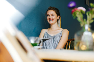 Cheerful young woman looking away while sitting at cafe