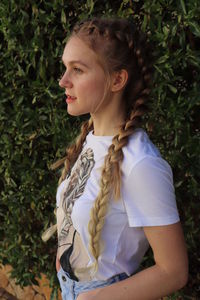 Young woman looking away while standing against plants