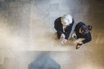 High angle view of senior businesswoman showing mobile phone to coworker while standing in office