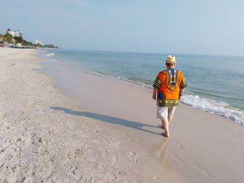 Rear view of senior man walking at beach against clear sky