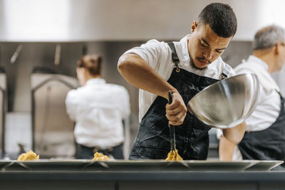 Focused young male chef plating pasta in plate at commercial kitchen