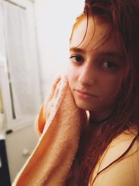 Close-up portrait of young woman wiping face with towel in bathroom