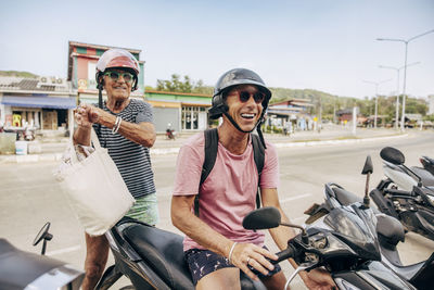 Senior man standing near boyfriend sitting on motorcycle at street road