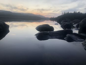 Rocks in lake against sky during sunset
