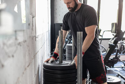 Concentered male athlete taking heavy barbell weight while training in modern gym