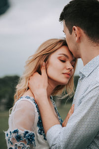 Man kissing woman while standing against sky