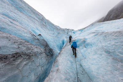 Rear view of hikers climbing glacier against sky