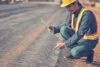 Side view of engineer using digital tablet while crouching on road