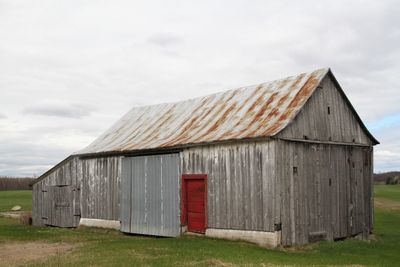 Old barn with red door on field against sky
