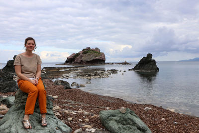 Portrait of woman sitting on rock at sea shore against sky