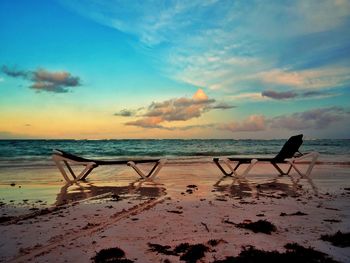 Deck chairs on beach against sky during sunset