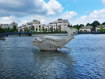 Boats moored in river by buildings in city against sky