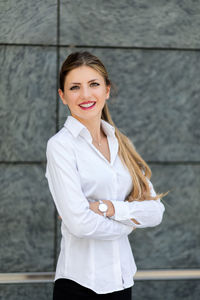 Portrait of a smiling young woman standing against wall