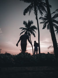 Silhouette couple standing by palm trees against sky during sunset