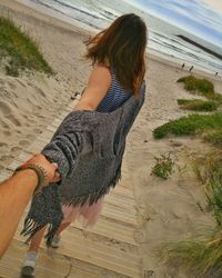 Cropped image of man holding woman hand at beach