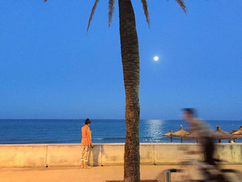 Rear view of man standing at beach against clear blue sky