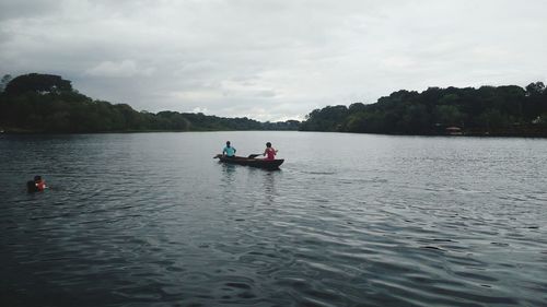 People on boat in lake against sky