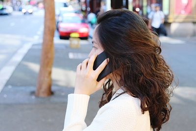 Side view of woman talking on phone on street in city