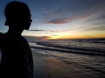 Side view of silhouette woman standing at beach against sky during sunset