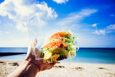 Close-up of hand holding drink at beach against sky