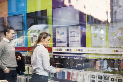 Saleswoman assisting man in buying phone cover seen through glass