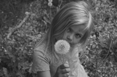 Portrait of girl holding dandelion on field