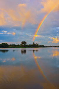 Rainbow over lake against sky during sunset