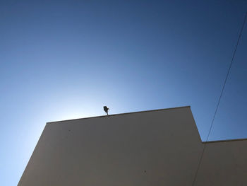 Low angle view of silhouette man standing against building against clear blue sky