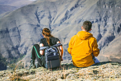 Rear view of couple sitting on cliff against mountains