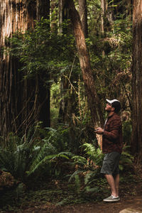 Side view of man standing in forest operating a drone aircraft